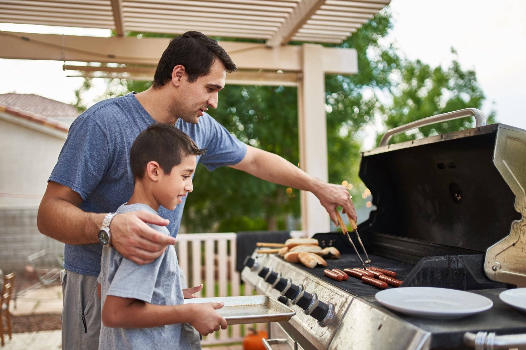 father teaching son how to grill hot dogs and bonding