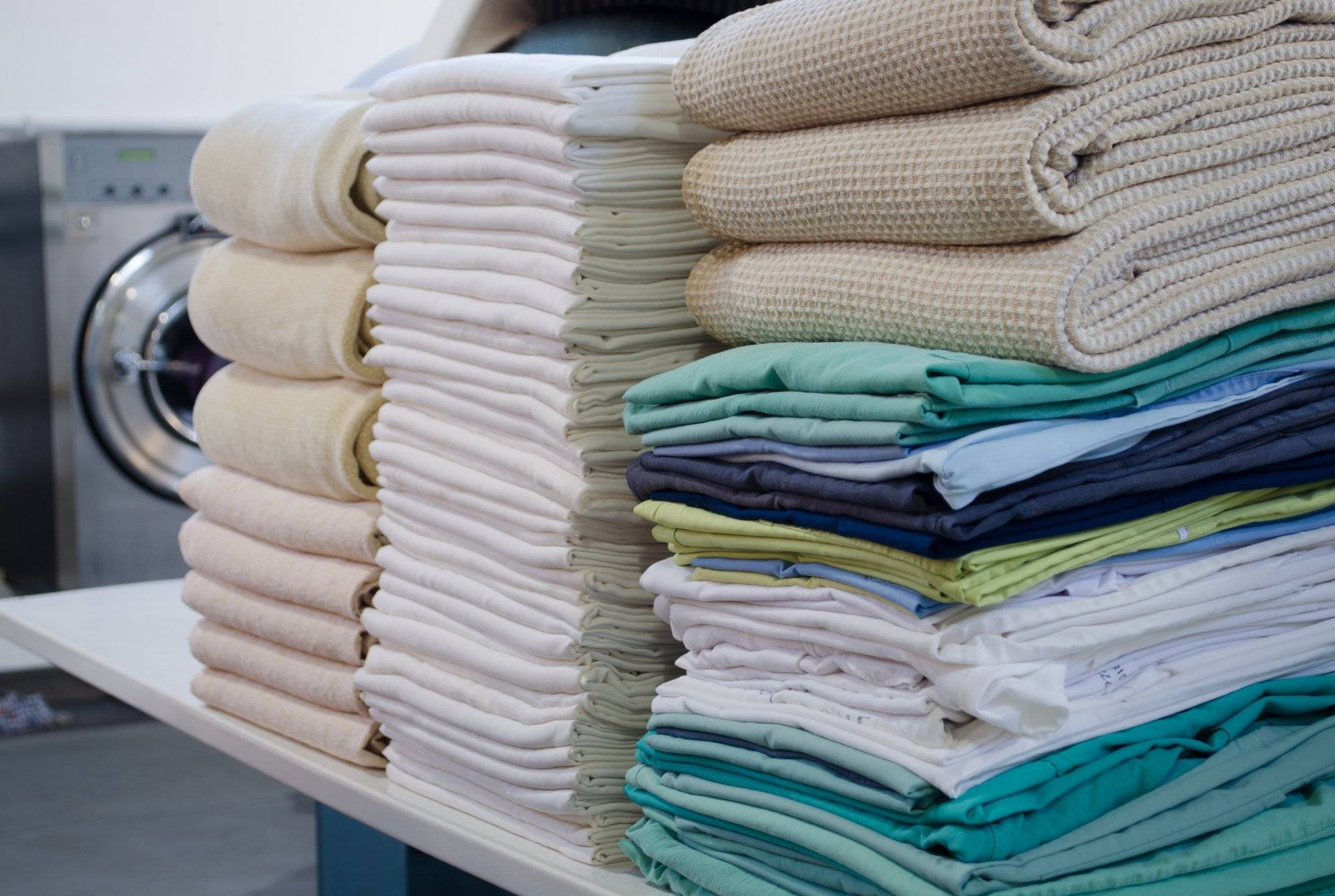 Stack of folded clean sheets, surgical clothes and industrial iron in an industrial laundry. Cleaning and ironing service for hospitals and clinics. Selective focus. Stack of folded clean sheets, surgical clothes and industrial iron in an industrial laundry. Cleaning and ironing service for hospitals and clinics. Selective focus.